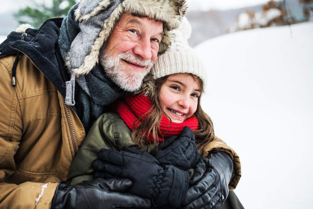 A portrait of senior grandfather and a small girl in snow on a winter day.