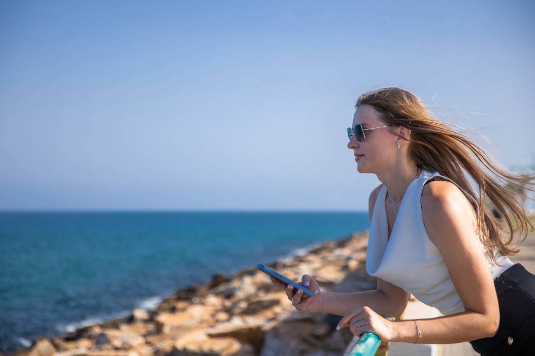 A young stylish woman communicates on a smartphone against the backdrop of a city seascape