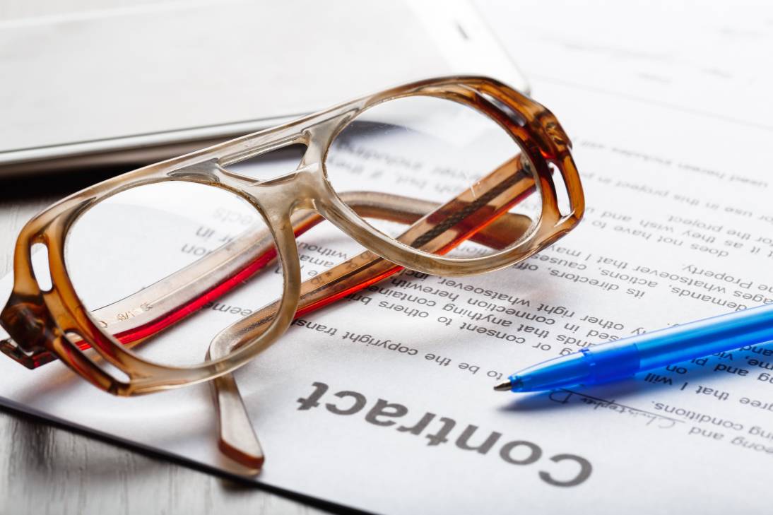 Contract paperwork with glasses and a blue pen on a wooden table