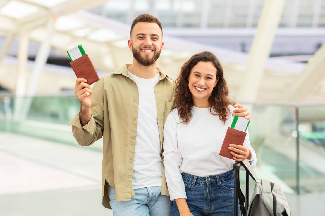 Couple smiling with travel documents at airport.