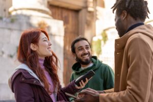 Diverse friends smiling and chatting outdoors, multicultural group using smartphones in city