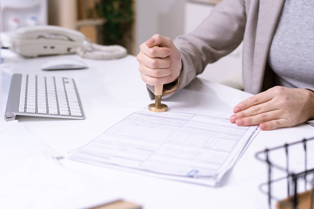 Hands of young female office worker putting seal on financial document