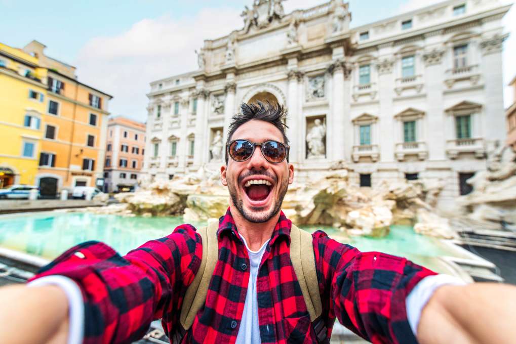 Happy young tourist taking selfie in front of Trevi Fountain during summer vacation in Italy