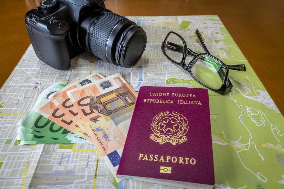 Italian and Brazilian passports on city map with euro bills money, camera and glasses