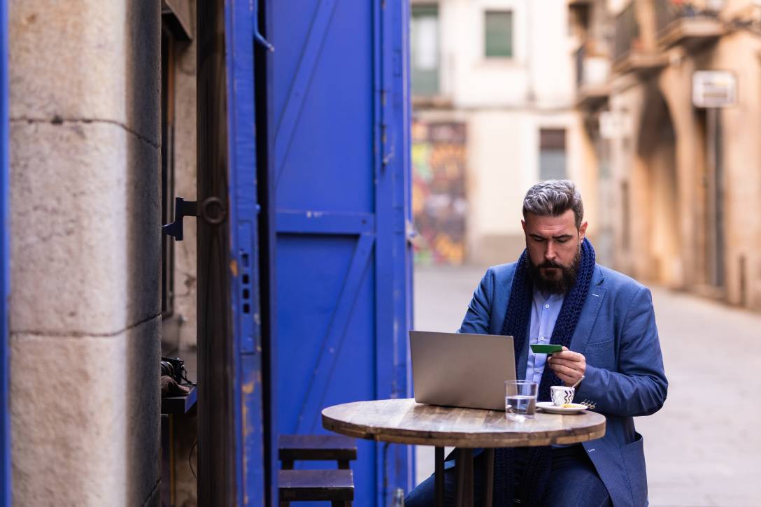 Man sitting in cafe outside using his laptop and credit card