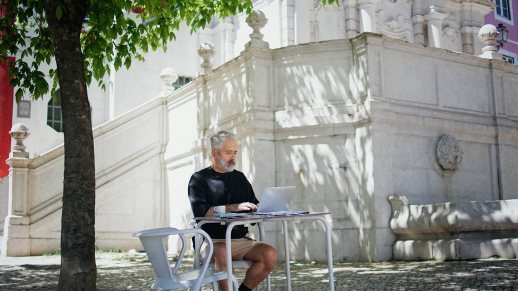 Mature businessman drinking coffee at street cafe. Focused senior working laptop