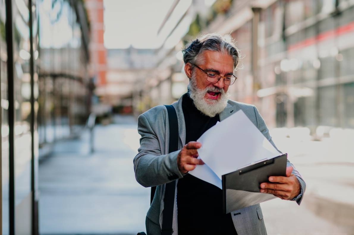 Senior businessman standing outside and reading requirements on a clipboard.