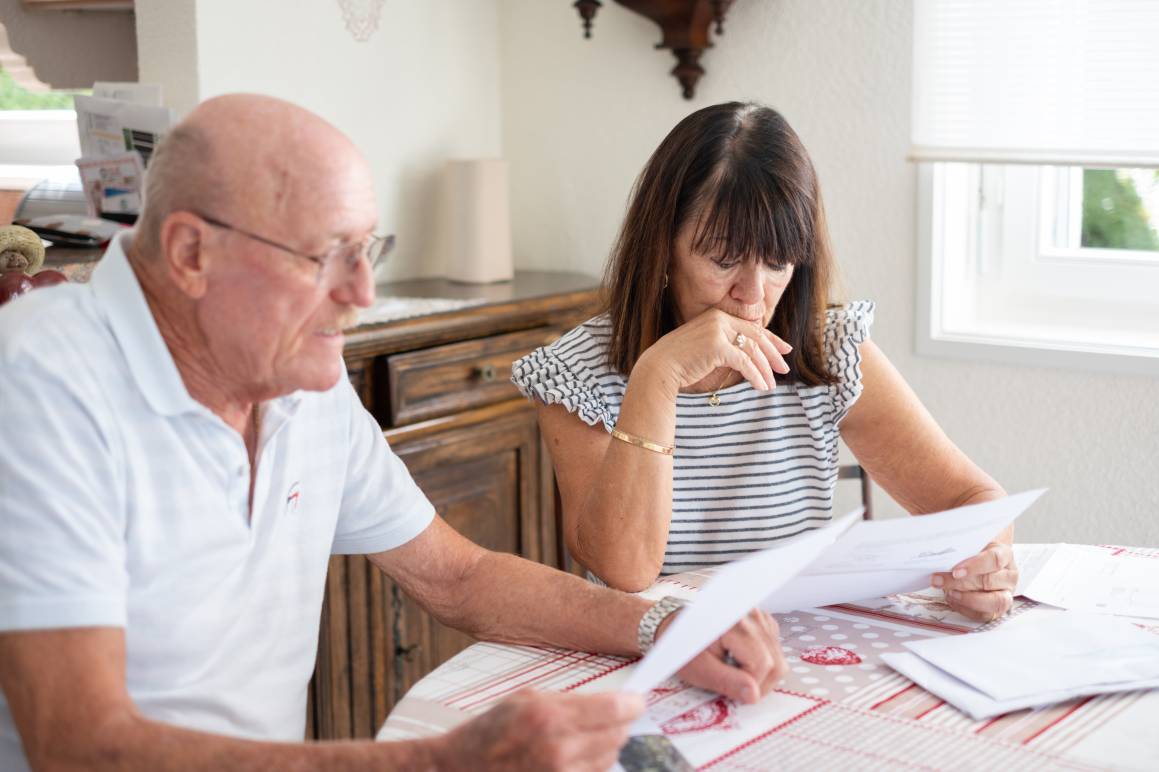 Senior couple sitting at home table with paper documents.