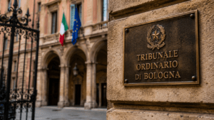 Bronze plaque reading “Tribunale Ordinario di Bologna” mounted on a stone wall outside the Bologna courthouse, with the Italian and European Union flags visible in the softly blurred background.
