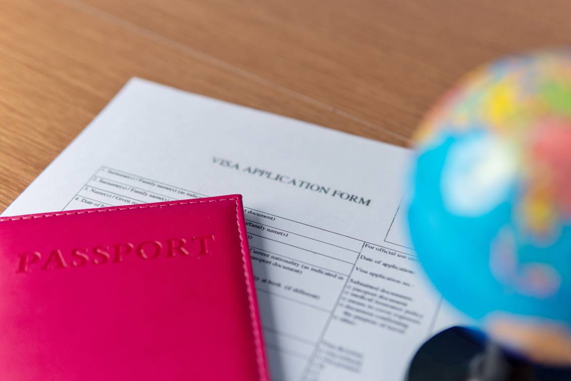 A visa application form, a red passport, and a globe