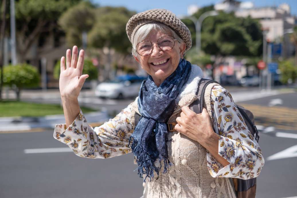 Happy senior woman traveler in sunny city centre expressing positivity, good mood, holding backpack