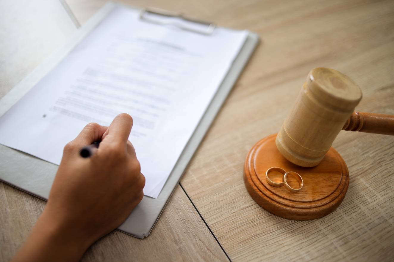 Person Signing Document with a Judge Gavel and Wedding Rings on The Table
