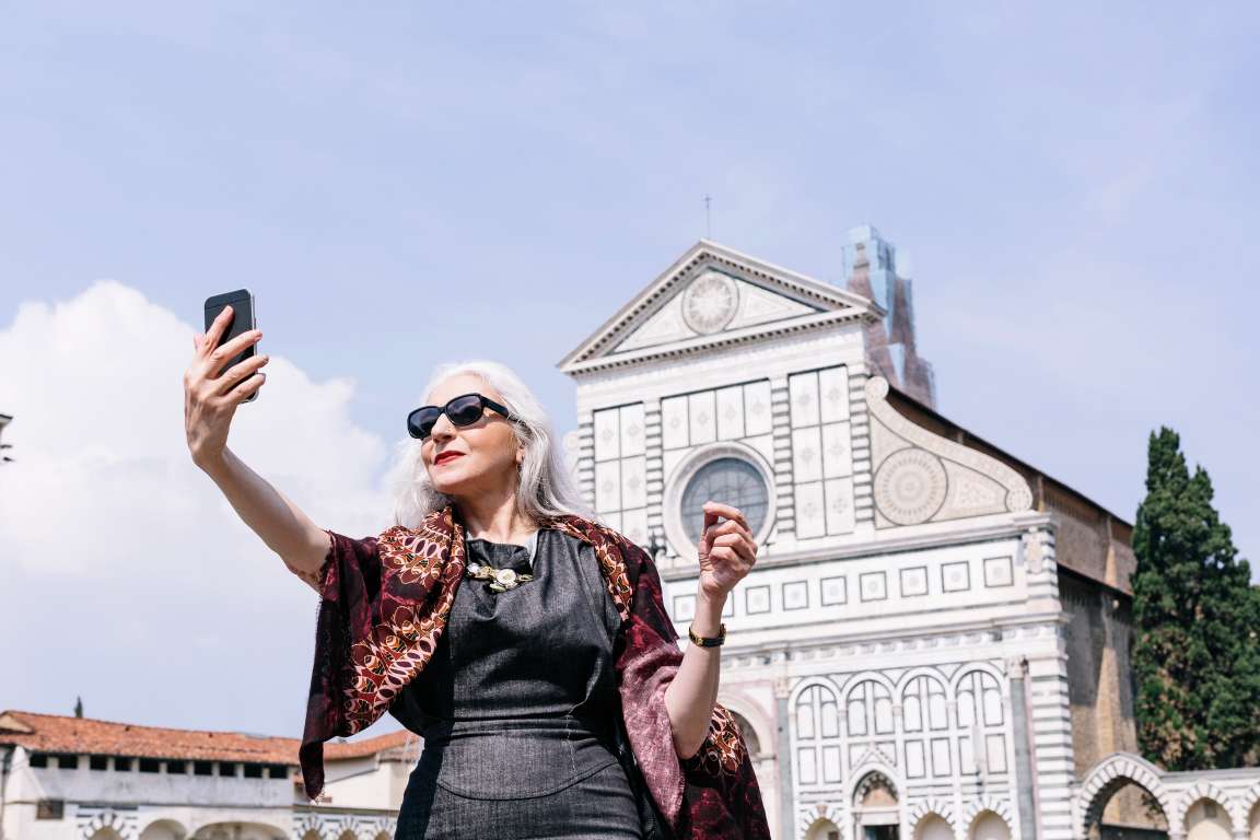 Stylish mature woman taking selfie in front of Santa Maria Novella church, Florence, Italy