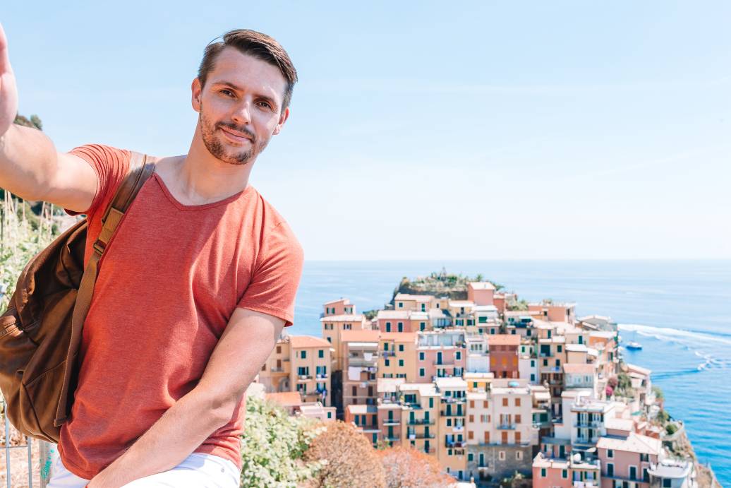 Young tourist in sunglasses taking selfie with scenic view of Manarola, Cinque Terre, Liguria, Italy